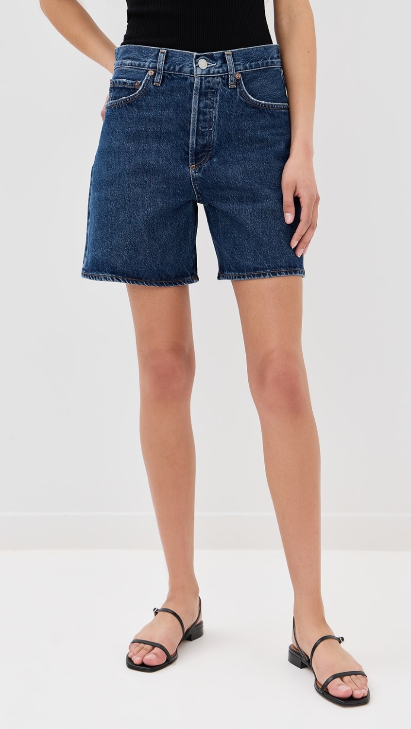 Dark blue denim mid-thigh denim shorts on a model.