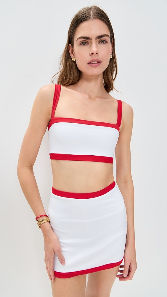 White sports bra and active skort set with red outline on a model.