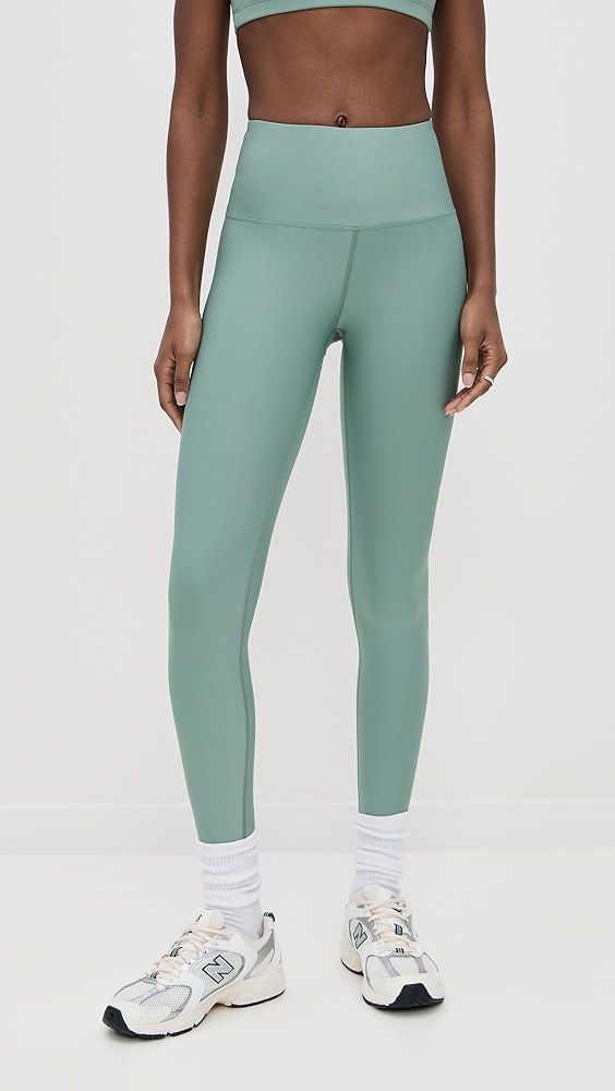 Sage green shiny leggings on a model, which is one of the trendy activewear pieces.